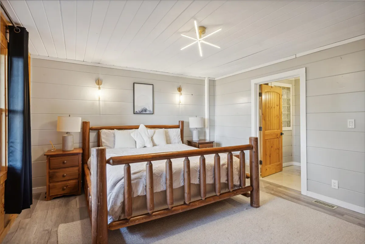 A tranquil master bedroom featuring a log bed, wooden nightstands, rustic artwork, and a doorway leading to a private ensuite. Soft lighting and natural tones create a restful atmosphere, ideal for peaceful sleep and gentle awakenings.