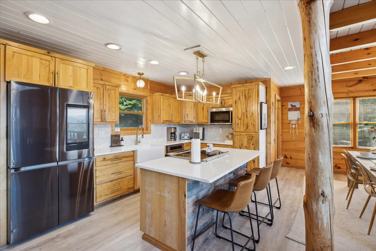 A modern, open-concept kitchen with a central island, stainless steel refrigerator, contemporary lighting, wood cabinetry, and a seamless flow into the adjacent dining space. The arrangement is perfect for cooking, socializing, and family gatherings.