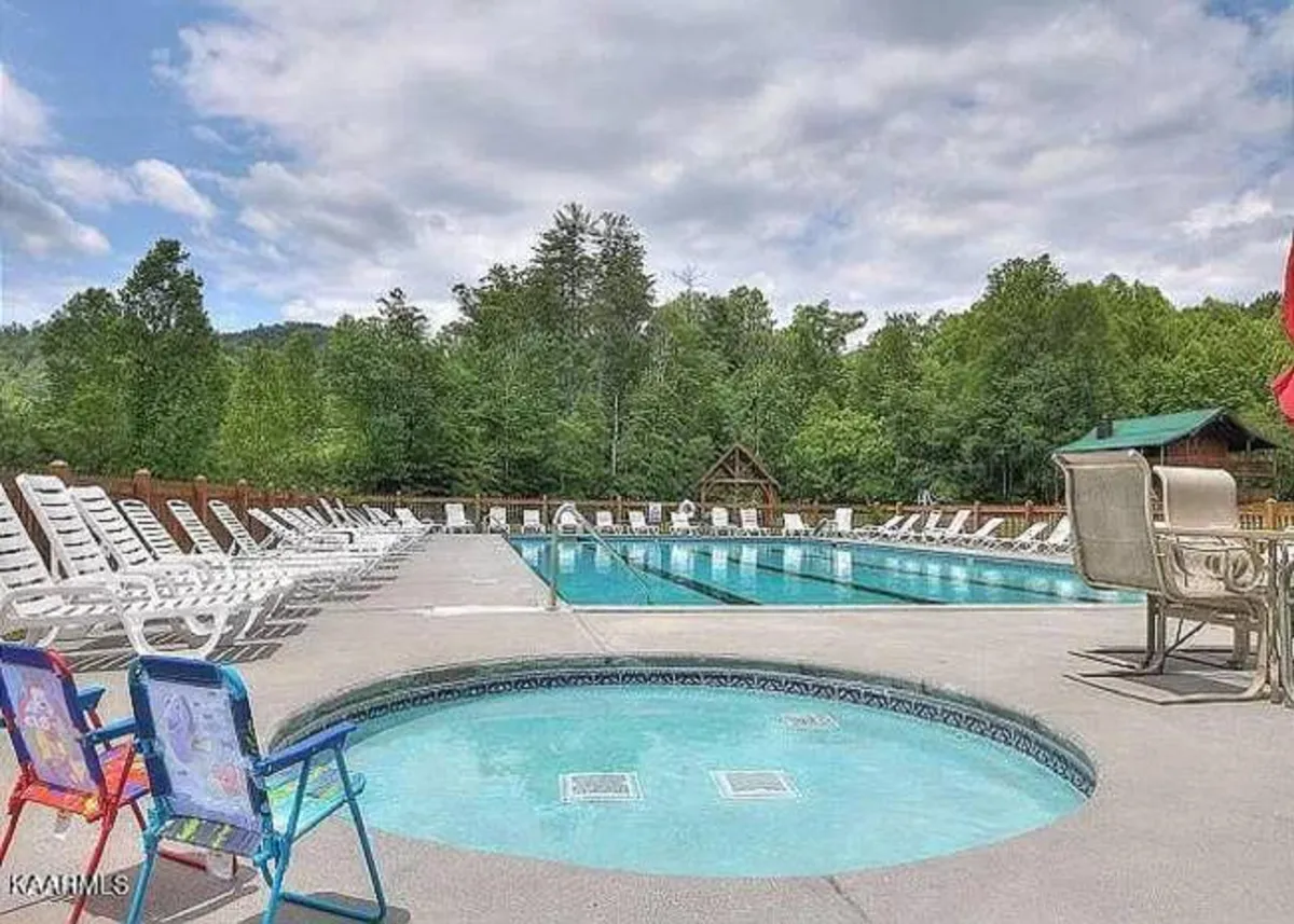 A tranquil community pool area with a hot tub, lounge chairs, and abundant greenery, suggesting a space for relaxation, swimming, and socializing. The serene atmosphere is ideal for families and groups seeking fun just steps away from their retreat.