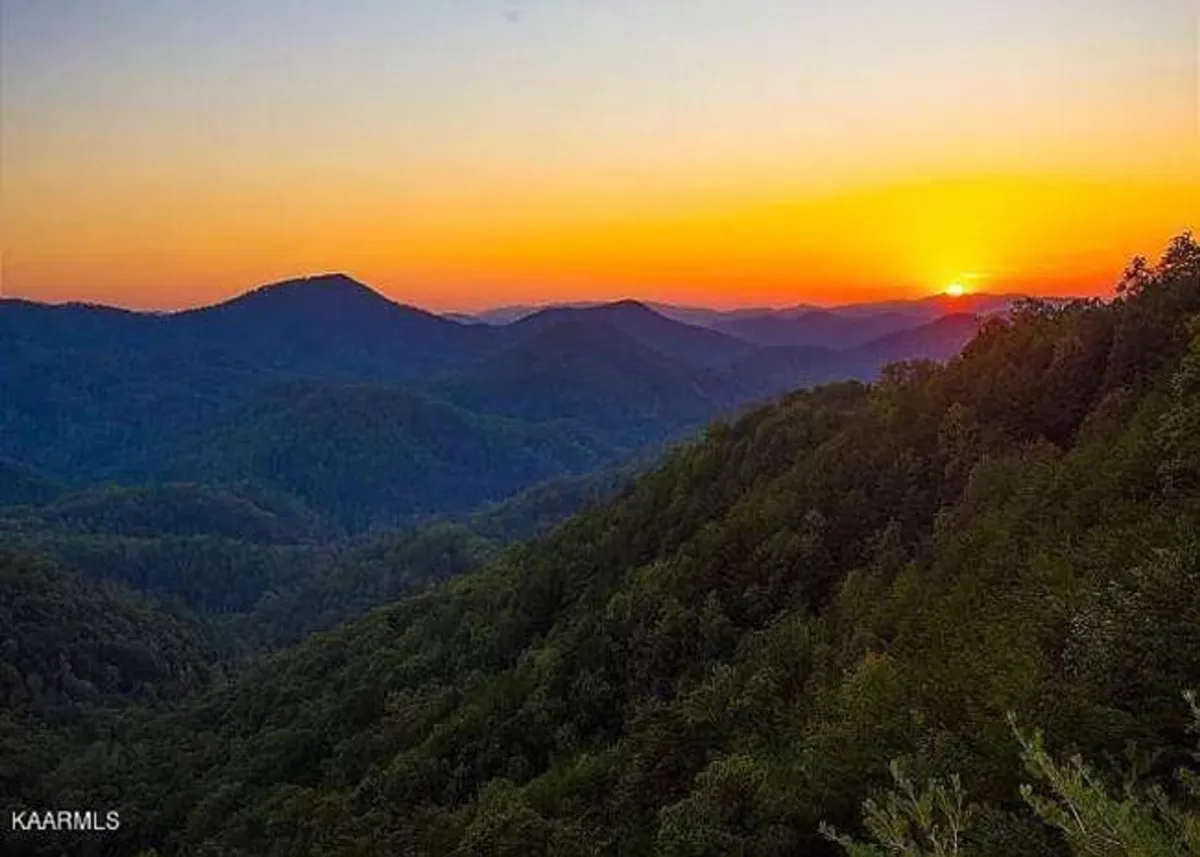 A wide, scenic view of rolling mountain ranges bathed in the gentle glow of sunset, surrounded by lush greenery. The composition invites outdoor exploration, peaceful walks, and moments of reflection amidst nature.