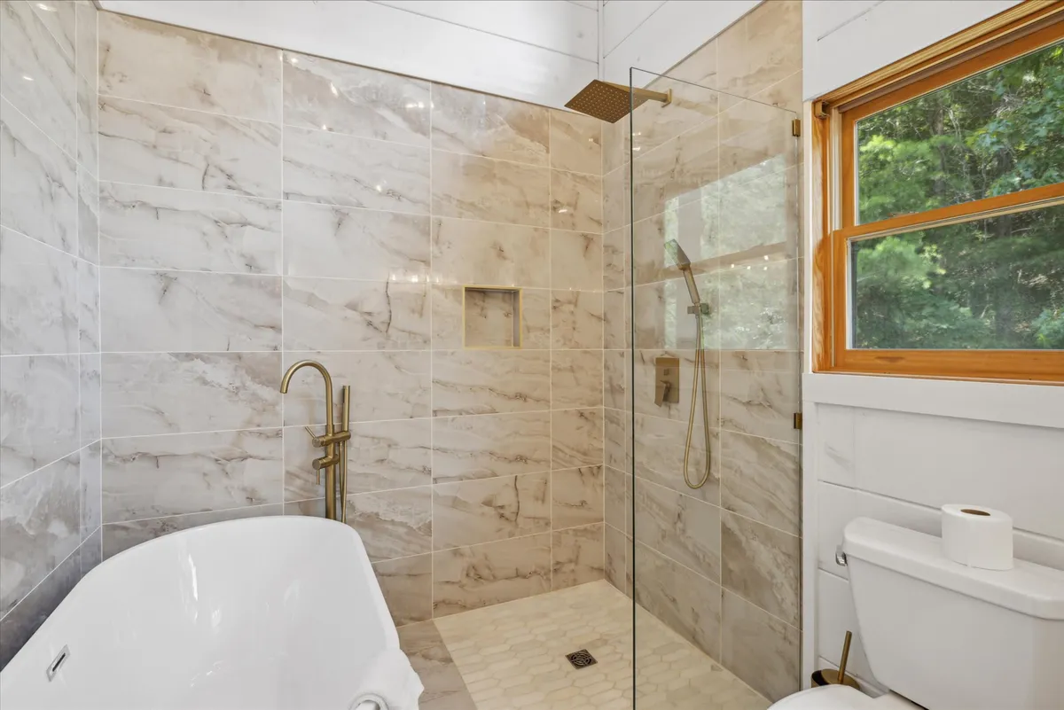 A luxurious ensuite bathroom with a freestanding soaking tub, glass-enclosed shower, and elegant gold fixtures. The space exudes tranquility with its clean lines and spa-like design, ideal for restorative baths and self-care rituals.