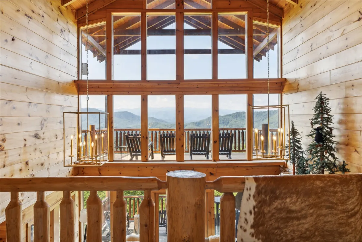 An inviting interior space featuring large windows that open to a balcony with seating, offering breathtaking mountain views. Hanging light fixtures cast a cozy glow, and the layout encourages relaxation or socializing with loved ones.