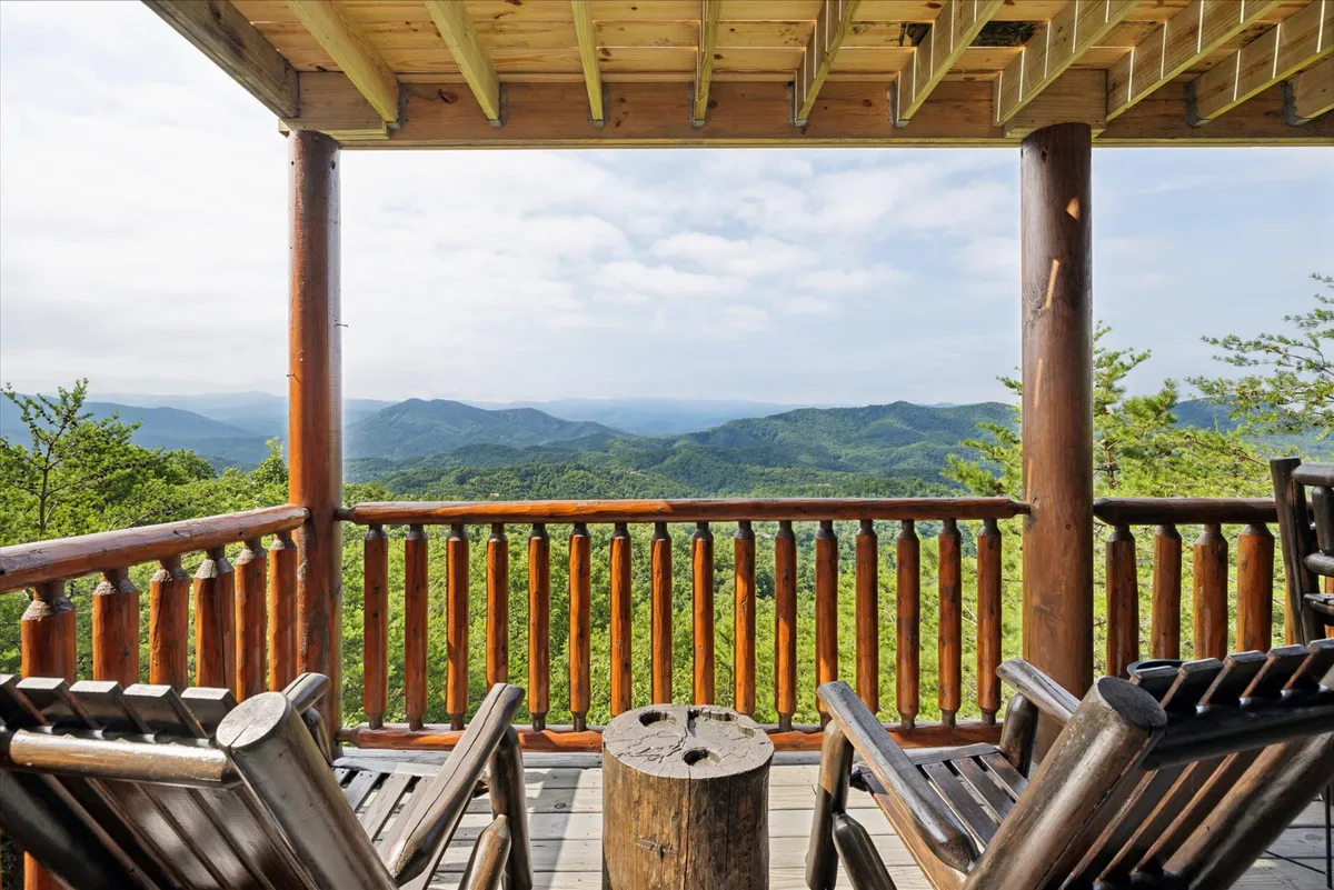 An inviting exterior porch scene with classic wooden rocking chairs lined up along a sturdy wooden railing, all set against the backdrop of a sweeping mountain view. The atmosphere is tranquil, with soft natural lighting ideal for relaxation, meditation, or quiet reflection outdoors.