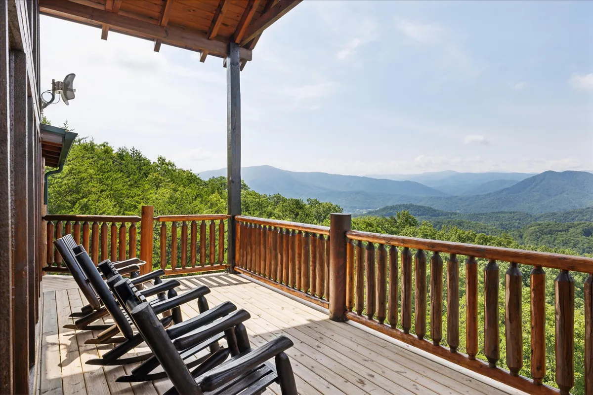 The image showcases a cozy exterior porch with classic rocking chairs overlooking a breathtaking mountain view. The log railing and natural surroundings establish an inviting spot for relaxation, reading, or sipping coffee while soaking in the scenic landscape.
