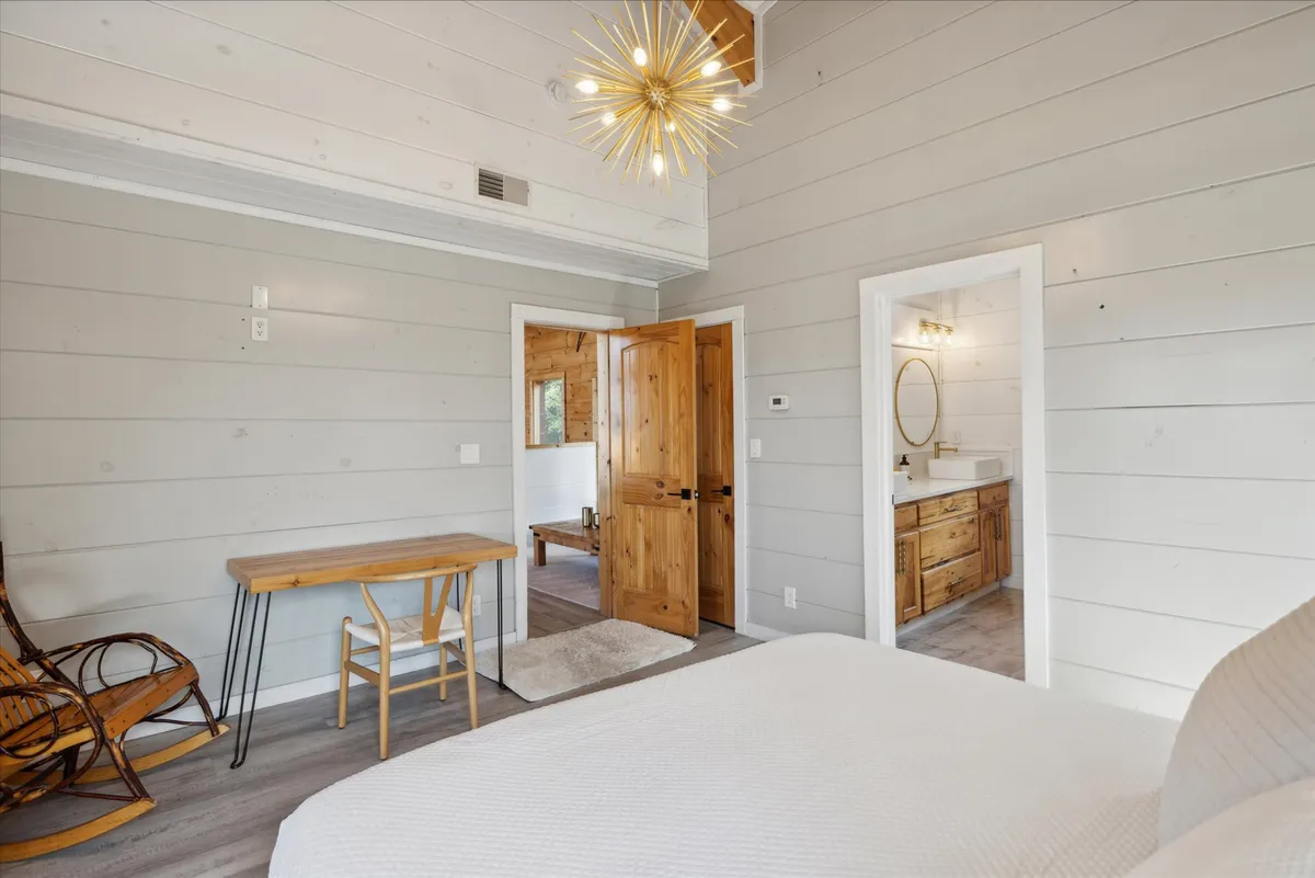 A cozy and modern bedroom featuring a comfortable bed, stylish wooden furniture, a well-lit work desk, and convenient access to the chic bathroom. There’s ample space for both rest and productivity, with a desk setup ideal for remote work.