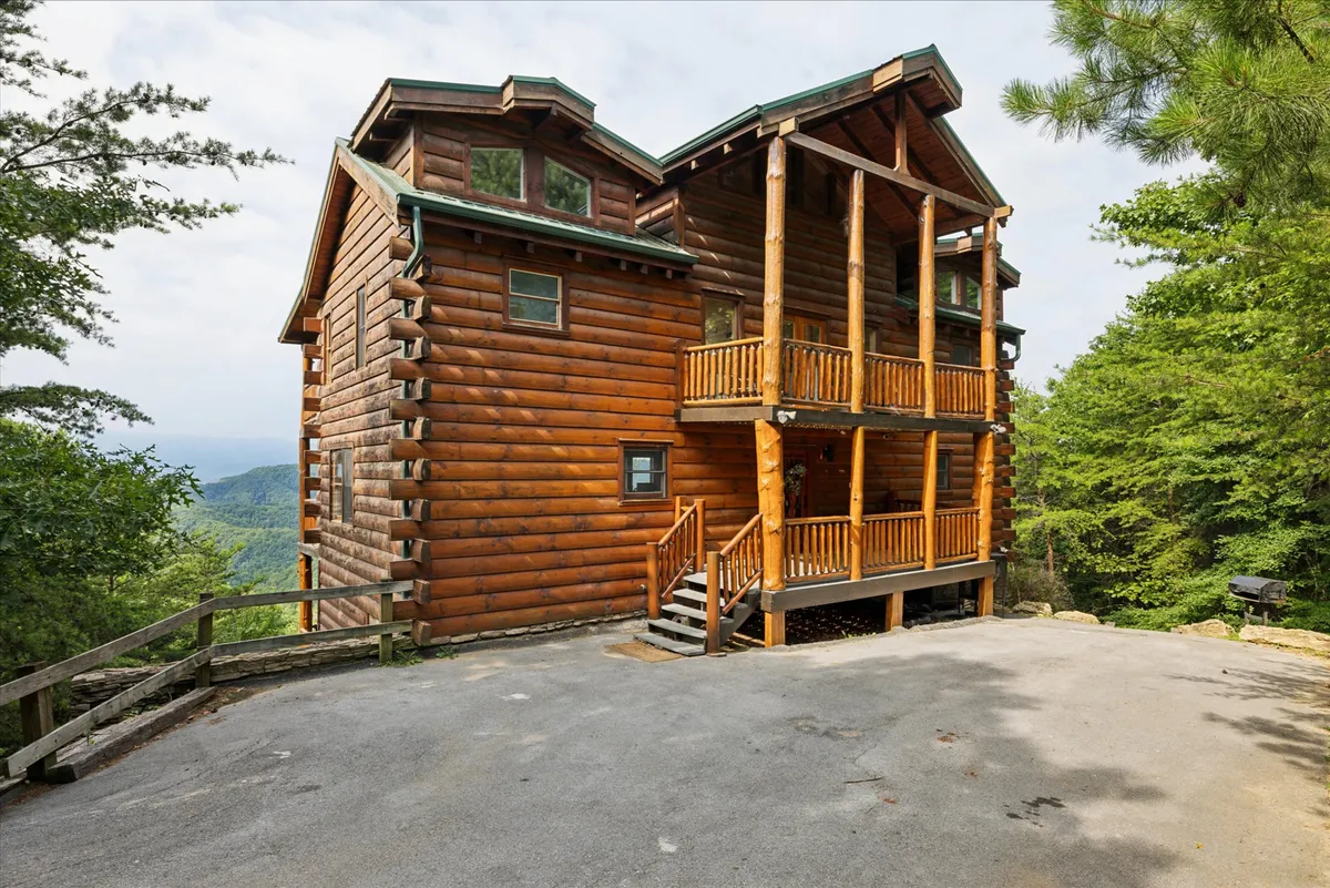 A broad exterior shot of the log cabin, surrounded by lush trees and set against a panoramic mountain backdrop. The cabin features inviting balconies and porches with railings, providing a seamless transition from indoor comfort to outdoor adventure. The scene evokes a sense of tranquility and proximity to nature, ideal for launching daily explorations or unwinding after an active day.